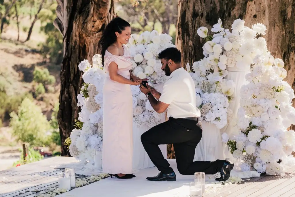 couple proposing with white flowers in the background